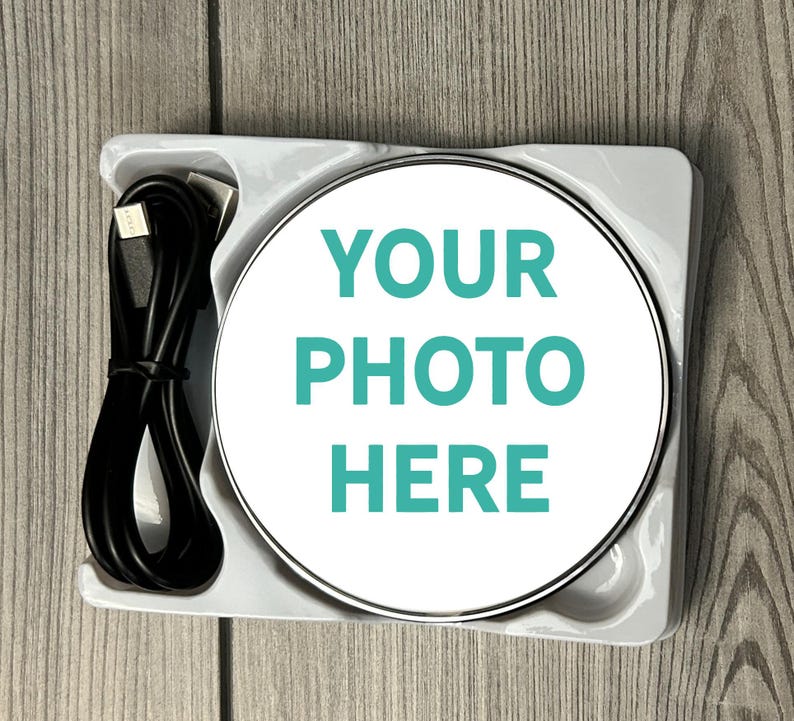 May include: A white wireless charging pad with a silver trim. The pad has the text "YOUR PHOTO HERE" printed on it in teal.