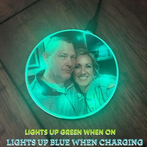 May include: A round wireless charging pad with a photo of a couple printed on it. The charging pad lights up green when on and blue when charging.