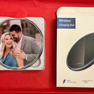 May include: A white wireless charging pad with a black charging surface and a photo of a couple on the front. The charging pad is 15W and compatible with Qi-enabled devices. The text "Wireless Charging Pad" and "15W" are printed on the box.