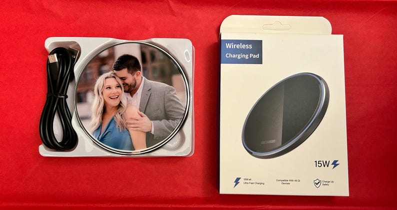May include: A white wireless charging pad with a black charging surface and a photo of a couple on the front. The charging pad is 15W and compatible with Qi-enabled devices. The text "Wireless Charging Pad" and "15W" are printed on the box.
