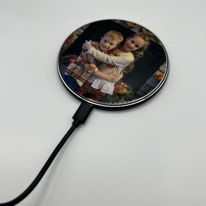 May include: A round wireless charging pad with a photo of two children hugging. The charging pad has a silver rim and a black cord.