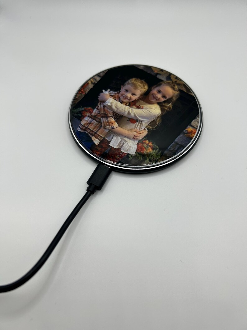 May include: A round wireless charging pad with a photo of two children hugging. The charging pad has a silver rim and a black cord.