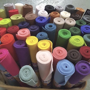 Pode incluir: Uma coleção de feltro enrolado em várias cores, incluindo vermelho, amarelo, verde, azul e roxo. Os rolos são bem enrolados e exibidos em uma cesta, mostrando a diversa paleta de cores e texturas do material.
