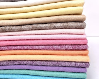 May include: A stack of rectangular felt sheets in various colors including gray, white, yellow, beige, pink, purple, orange, lavender, teal, and light blue. The sheets are layered horizontally, showing the textured, fibrous surface of the material.