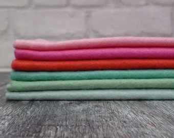Puede incluir: Pila de seis cuadrados de tela de fieltro en varios tonos de rosa, naranja y verde. El fieltro está doblado cuidadosamente y dispuesto en un patrón de arcoíris.