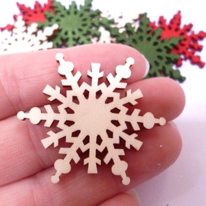 Pode incluir: Um close-up de um ornamento de floco de neve de madeira. O floco de neve é marrom claro e tem um design detalhado. Tem aproximadamente 5 cm de diâmetro.