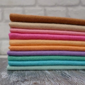 May include: A stack of ten felt fabric squares in various pastel colours, including brown, beige, pink, orange, purple, green, turquoise, and light green.