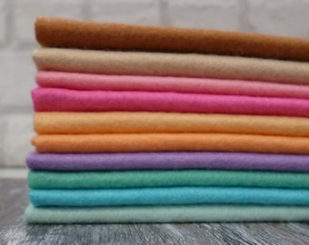 Puede incluir: Una pila de diez cuadrados de tela de fieltro en varios colores pastel, incluyendo marrón, beige, rosa, naranja, morado, verde, turquesa y verde claro.