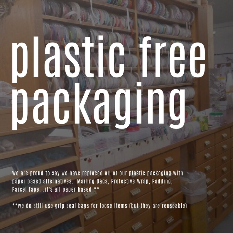 May include: A sign with the text "plastic free packaging" in white letters on a black background. The sign is in front of a wooden shelf filled with rolls of colorful ribbon.