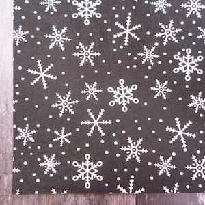 May include: A dark gray fabric with a repeating pattern of white snowflakes and small white dots. The snowflakes vary in size and design, creating a winter-themed textile.
