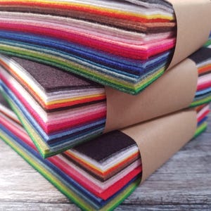 May include: Bundles of colourful felt sheets in a variety of shades, including red, pink, blue, green, and brown, are wrapped with brown paper. The felt appears to be of high quality, with a soft texture and vibrant colours. Suitable for craft projects.