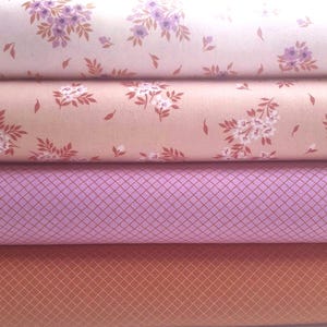 Può includere: Quattro rotoli di tessuto impilati. Il rotolo superiore è rosa chiaro con motivi floreali viola. Il secondo rotolo è pesca con motivi floreali bianchi. Il terzo rotolo è viola chiaro con un motivo a griglia. Il rotolo inferiore è arancione con un motivo a griglia.