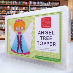 May include: A white box with a green and white polka dot background. The box contains a felt angel tree topper kit. The kit includes all the materials needed to make a felt angel tree topper. The box has the text "Sew Your Own Angel Tree Topper" and "designed by paper-and-string" on it.
