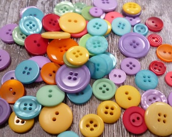 Puede incluir: Surtido de botones coloridos en varias formas y tamaños. Los botones están hechos de plástico y tienen un acabado liso y brillante. Los colores incluyen rojo, naranja, amarillo, verde, azul, morado y blanco.