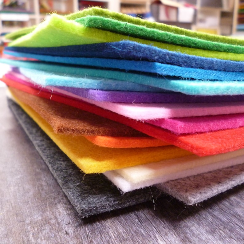Puede incluir: Una pila de hojas de fieltro de colores en varios tonos de verde, azul, morado, rosa, rojo, naranja, amarillo, blanco y gris. Las hojas de fieltro est&aacute;n dispuestas en un patr&oacute;n de arco&iacute;ris.