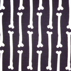 Può includere: Primo piano di un tessuto con un motivo ripetuto di forme di ossa bianche su uno sfondo blu navy scuro. Le ossa sono orientate verticalmente e uniformemente distanziate, creando un contrasto sorprendente.