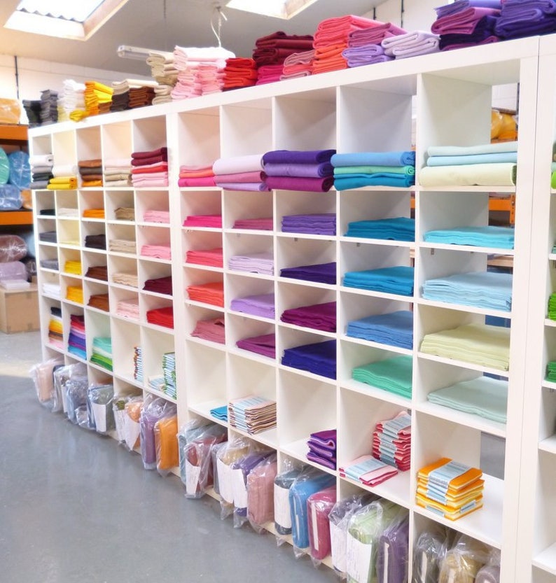 May include: A white shelving unit filled with stacks of colorful felt fabric squares. The shelves are organized by color, with each shelf containing a different shade of felt.