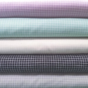 May include: A stack of fabric rolls in various pastel colors, including lavender, mint green, white, navy, and light gray. Each roll features a white grid pattern, creating a textured appearance. The fabric appears to be cotton or a similar material.