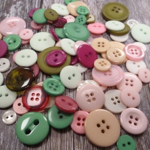 Puede incluir: Surtido de botones coloridos de diferentes formas y tamaños, incluyendo rosa, verde, marrón y blanco. Los botones son de plástico y tienen un acabado liso.
