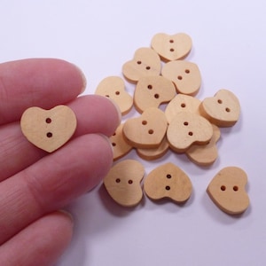 Könnte beinhalten: Ein Haufen von 16 naturfarbenen, herzförmigen Knöpfen aus Holz mit jeweils zwei Löchern. Die Knöpfe sind hellbraun und haben eine glatte Oberfläche.