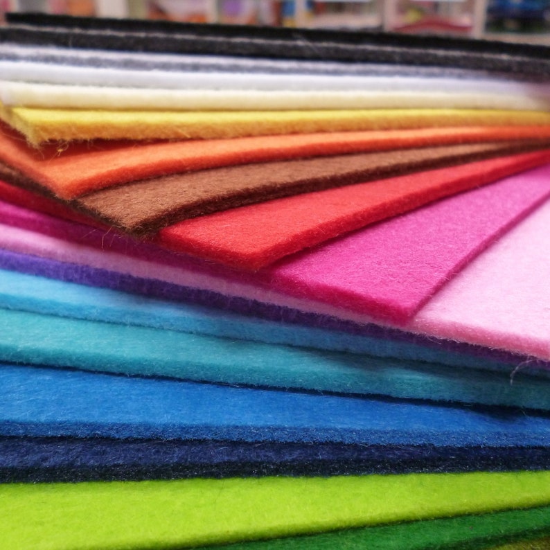 Puede incluir: Una pila de hojas de fieltro de varios colores, incluyendo negro, blanco, amarillo, naranja, rojo, marr&oacute;n, rosa, morado, azul, verde y verde oscuro.