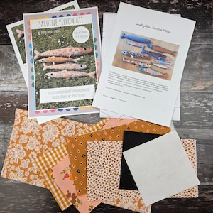 Puede incluir: Un kit de cojín de sardina de Paper and String, con un patrón impreso a tamaño completo e instrucciones fotográficas. El kit incluye piezas de tela en tonos naranja, rosa y marrón, además de un cuadrado blanco y negro. El kit hace cuatro sardinas.