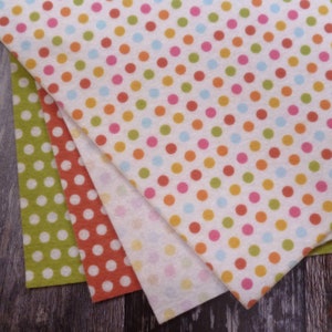 May include: Four pieces of fabric with different polka dot patterns. The fabric is white with orange, pink, blue, and green polka dots. The fabric is folded in a triangle shape.