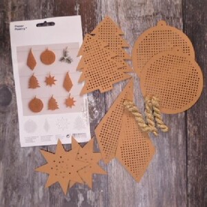 May include: A set of 10 brown paper craft ornaments with a grid pattern for cross-stitching. The ornaments include a star, a tree, a bell, and other shapes. The paper is packaged with a white card that says "Paper Poetry".