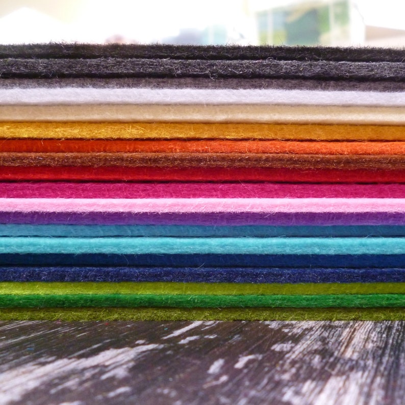 Puede incluir: Una pila de hojas de fieltro de varios colores, incluyendo negro, blanco, beige, amarillo, naranja, rojo, marr&oacute;n, rosa, morado, azul, verde y azul oscuro.