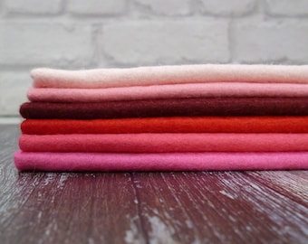 Puede incluir: Una pila de seis hojas de fieltro en varios tonos de rosa y rojo. Las hojas de fieltro están dispuestas de la más clara a la más oscura, con la hoja más clara en la parte superior y la hoja más oscura en la parte inferior.