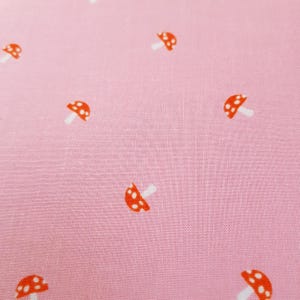 Peut inclure: Tissu rose clair avec un motif répété de petits champignons rouges à tiges blanches. Les champignons sont répartis sur le tissu, créant un design fantaisiste. Le tissu a un aspect légèrement texturé.