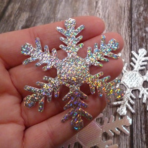 May include: Silver glitter snowflake with a holographic finish. The snowflake is cut out of paper and has a textured surface.