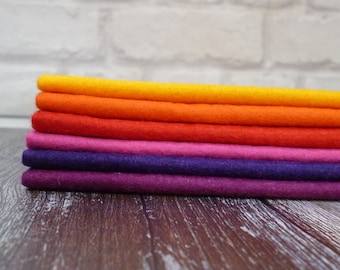 Puede incluir: Una pila de seis hojas de fieltro en un degradado de colores arcoíris, comenzando con naranja y pasando a morado. Las hojas de fieltro están dispuestas en una pila ordenada sobre una superficie de madera.