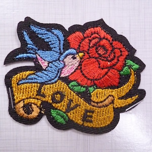 May include: Embroidered iron-on patch featuring a blue bird flying over a red rose with green leaves and a gold banner that reads "LOVE".