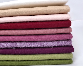 Puede incluir: Una pila de diez láminas rectangulares de fieltro en un degradado de colores que incluye blanco, beige, rosa claro, rojo oscuro, rosa viejo, magenta, lavanda, morado oscuro, verde oliva claro y verde oliva oscuro con textura fibrosa.