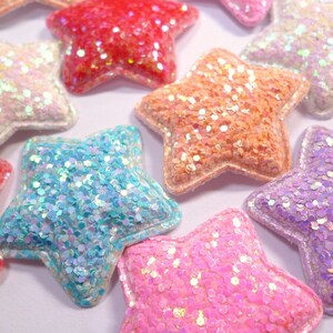 May include: Assortment of five glittery star-shaped embellishments in various colours, including pink, blue, orange, and white.