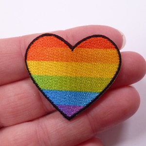 May include: A rainbow heart-shaped patch with red, orange, yellow, green, blue, indigo, and violet stripes. The patch is embroidered with a black outline.