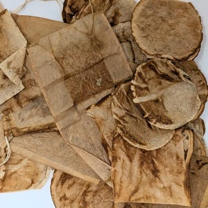 May include: A close-up of used tea bags and coffee filters, stained with brown tea and coffee. The tea bags are various shapes, including rectangular and square, some with strings. The coffee filters are circular.