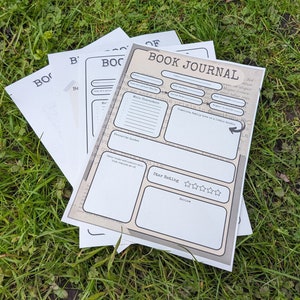 May include: A stack of white paper sheets featuring a printed book journal template. The top sheet has the title BOOK JOURNAL and includes sections for author, title, dates, main characters, favorite quotes, star rating, and a review.