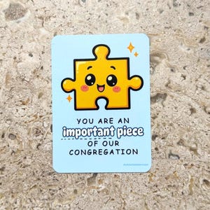 May include: A light blue card with a yellow puzzle piece graphic and the text "YOU ARE AN important piece OF OUR CONGREGATION". The puzzle piece has a smiling face and sparkles.