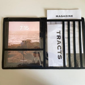 May include: Black folio-style organizer with a tablet displaying a beach scene and the time 7:15. The organizer has clear pockets and a section for a magazine and tracts. The word "TRACTS" is printed vertically.