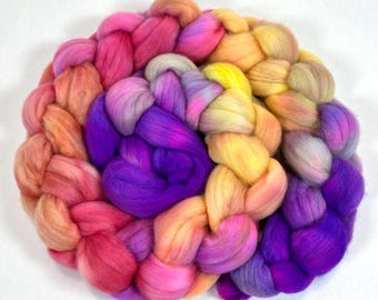 Può includere: Una treccia circolare di stoppino di lana tinta, che mostra uno spettro di colori. La lana presenta sfumature di rosa, viola, giallo e arancione. Lo stoppino intrecciato stretto presenta una texture attraente, ideale per lavori manuali.