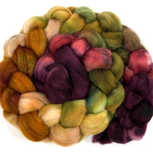May include: A braided bundle of colorful wool roving in shades of burgundy, green, gold, and cream. The wool is arranged in a circular shape, with the ends of the braids overlapping.