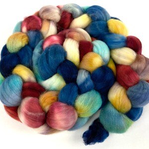 Pode incluir: Um novelo de fio trançado em tons de azul, amarelo, rosa e vermelho. O fio está disposto em forma circular, com as pontas do novelo visíveis.