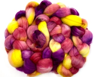 May include: A bundle of colorful wool roving in shades of yellow, pink, and purple. The roving is arranged in a loose, circular shape.