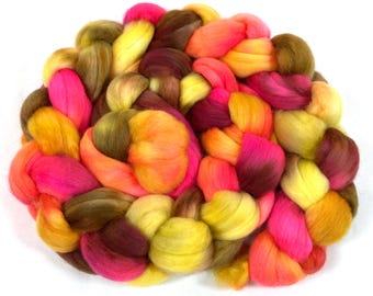 Può includere: Primo piano di un mucchio di lana cardata colorata in tonalità rosa, arancio, giallo e marrone. La lana è disposta in un motivo circolare, creando una visualizzazione visivamente accattivante e testurizzata.