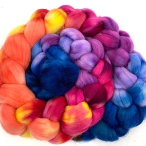 May include: A braided bundle of colourful wool yarn in shades of orange, yellow, pink, purple, and blue. The yarn is arranged in a spiral pattern.