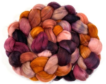 Può includere: Primo piano di un fascio intrecciato di stoppini di lana colorati. La lana è un mix di colori caldi, tra cui sfumature di arancione, rosa e viola. Le fibre sono morbide e soffici, ideali per progetti di arte tessile.