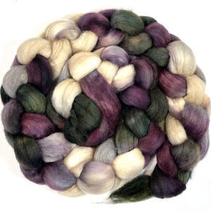 以下が含まれることがあります： さまざまな色の編み糸のクローズアップ。糸はクリーム、紫、緑、グレーの混合です。糸は太く、柔らかく見えます。糸は円形に配置されています。