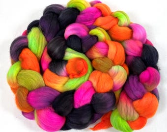 Può includere: Una vibrante e colorata treccia di stoppino di lana tinta. La fibra è un mix di colori vivaci, tra cui verde neon, rosa acceso, arancione, viola e nero. La lana è strettamente intrecciata, creando una fornitura artigianale strutturata e visivamente accattivante.